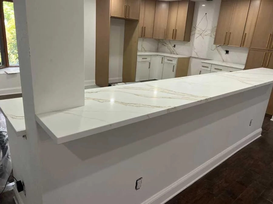White quartz countertop with gold and grey veining installed on a kitchen island, with matching backsplash and light wood cabinetry in the background